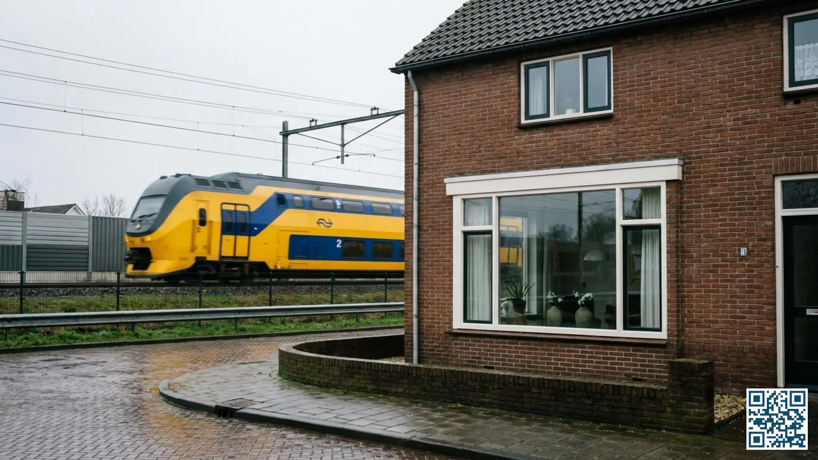 Nederlandse woning met nieuwe ramen direct naast het spoor terwijl een trein passeert op de achtergrond